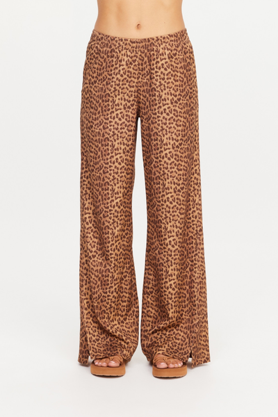 Front studio view of the Javan Juliet Pant in leopard print, styled with tan platform slide sandals. The image clearly displays the low-rise elasticated waist, relaxed wide-leg silhouette, and subtle side split hem details.