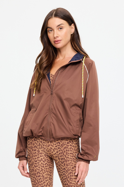 Side profile studio portrait of a model showcasing the Lila Zip Through Jacket in chocolate brown. This view displays the relaxed fit, clean raglan sleeve structure, cream piping running along the front armhole, and the elasticated wrist cuffs.