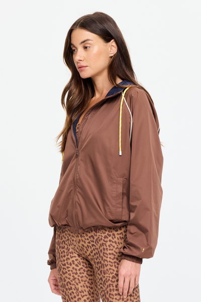 Rear studio view of a model wearing the Lila Zip Through Jacket. The shot highlights the contrast navy hood, the clean raglan sleeve design framed by cream piping, and the adjustable elasticated hemline designed to sit flat against leopard-print leggings.