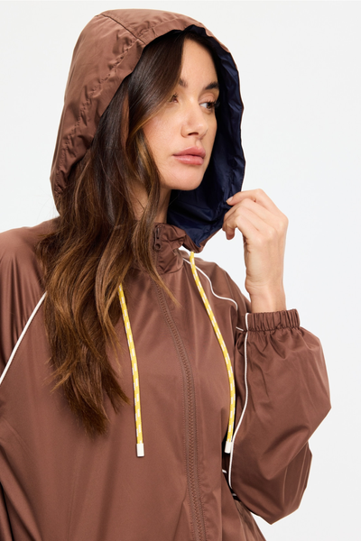 Close-up studio shot of a model wearing the hooded Lila Zip Through Jacket. The image highlights the hood lined in contrasting navy fabric, the high-zip collar, and the bright yellow drawstring with white aglets.