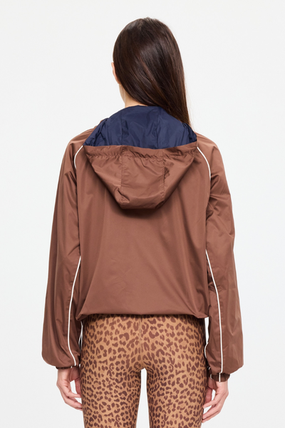 A woman shown from the back wearing a brown hooded jacket with a navy blue inner hood lining and white piping details, paired with leopard print leggings, against a plain light gray background.