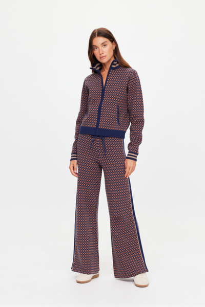 A full-length studio shot from the back showing a model wearing the high-waisted geometric star pattern knit trousers. The photo highlights the straight-leg drape down to the ankles, the clean rear profile, and the signature tonal embroidered arrow logo positioned centered on the back waistband.
