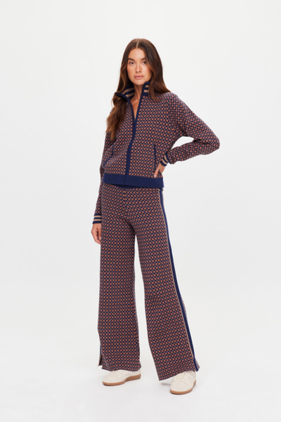 A full-length studio product shot from the back showing a model wearing the high-neck geometric star jacquard zip jacket. The photo emphasizes the clean pattern alignment across the shoulders and back panel, the relaxed fit, and the ribbed collar and hem trim accented with contrast tan stripes.