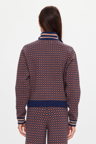 A full-length studio product shot from the back showing a model wearing the high-neck geometric star jacquard zip jacket. The photo emphasizes the clean pattern alignment across the shoulders and back panel, the relaxed fit, and the ribbed collar and hem trim accented with contrast tan stripes.