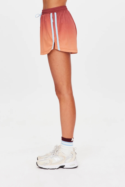 Full-length studio side view of a model wearing red-to-orange ombre run shorts with light blue mesh side tape, white crew socks, and beige sneakers.