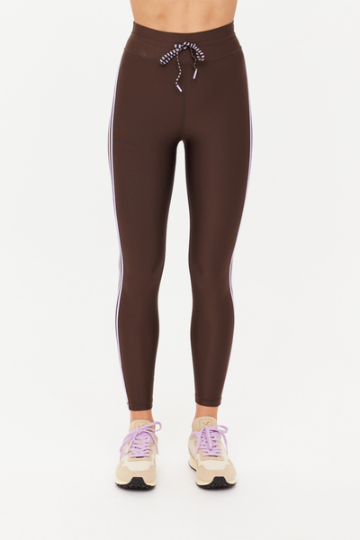 Front studio shot of the Oxford Midi Pant in cocoa brown. The image showcases the sleek compression fit of the Recycled Eco Tech fabric, the elasticated waistband with its striped lilac-and-black drawstring, and paired beige trainers with purple laces.