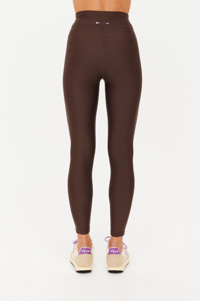 Rear view of a model wearing the cocoa brown Oxford 25-inch Midi Pant, showing the seamless seat construction and the signature small white arrow logo printed at the center of the waistband.