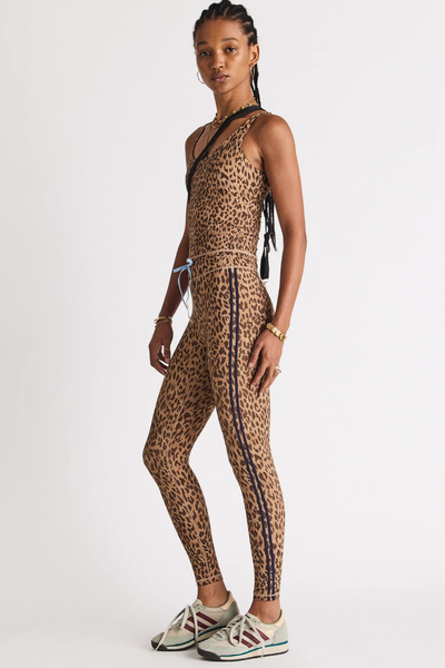 Full-length studio side profile portrait of a model wearing a complete leopard print activewear set consisting of a tank top and 25-inch midi pants with navy binding stripes.