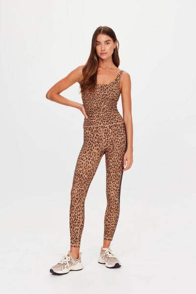 Studio full-length front view of a model wearing a complete leopard print activewear set including a scoop neck tank top and 25-inch midi leggings paired with sneakers.