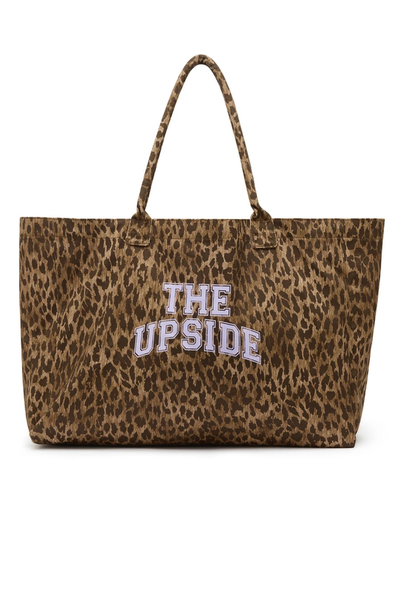 Studio front product view of a large organic cotton leopard print tote bag featuring dual soft tubular shoulder straps and a lilac "THE UPSIDE" varsity logo printed across the center.