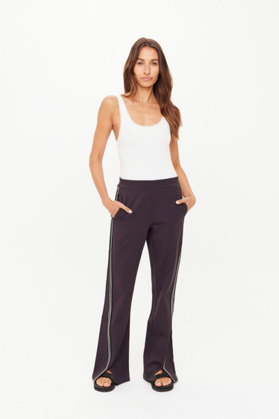 A full-length studio shot from the back showing the liquorice grey Petra Flare Pant, demonstrating the clean silhouette across the hips, the straight-to-flare leg line, and the subtle placement of the cream embroidered arrow logo.