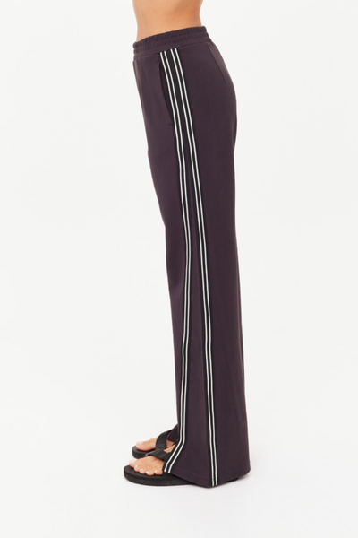 A side-profile studio photograph isolating the Petra Flare Pant on a model to highlight the full length of the black and cream striped tape running down the side seams, emphasizing the fluid drape of the Lenzing viscose soft suiting fabrication.