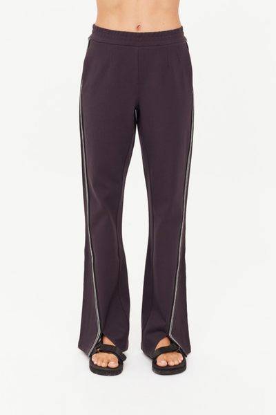 A full-length studio product shot capturing a model from the front wearing the grey liquorice Petra Flare Pant, paired with a white ribbed tank top. The shot showcases the relaxed, true-to-size fit, the flat elasticated waistband, integrated side seam pockets, and the statement front hem splits.
