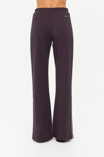 A full-length studio shot from the back showing the liquorice grey Petra Flare Pant, demonstrating the clean silhouette across the hips, the straight-to-flare leg line, and the subtle placement of the cream embroidered arrow logo.