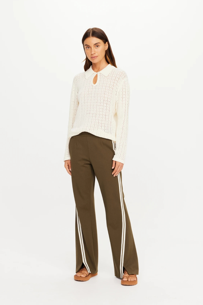 Full-length studio view of a model styled in The Upside Petra Flare Pant in Olive with a cream long-sleeve knit top and open-toe sandals.