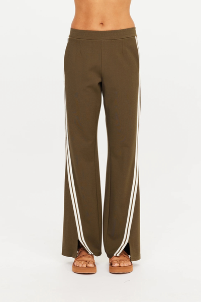 Full-length studio view of a model styled in The Upside Petra Flare Pant in Olive with a cream long-sleeve knit top and open-toe sandals.