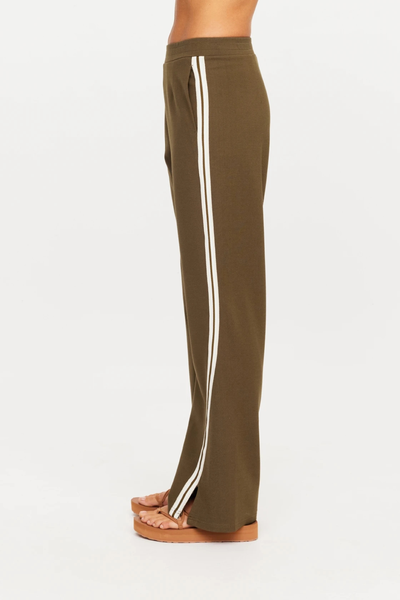 Side profile shot of a model wearing The Upside Petra Flare Pant in Olive, highlighting the cream side stripe tape and side seam pocket design.