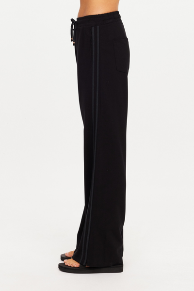Side profile shot of model wearing the black high-waisted Roma Pant by The Upside, highlighting the side seam detail and wide-leg length down to black sandals.
