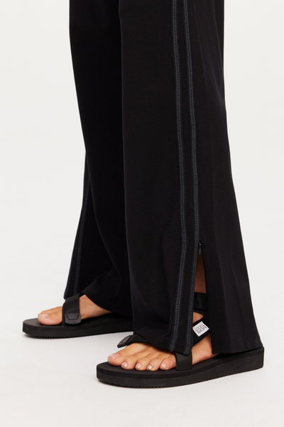 Close-up shot of the lower hem on The Upside Roma Pant in black, showing the unzipped invisible side seam detail over black sandals and knitted side tape.