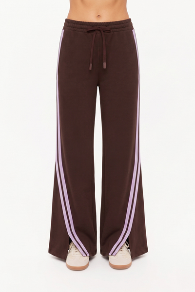 Front close-up studio shot of the Roma Pant from the waist down. The image highlights the comfortable elasticated waistband with a matching cocoa brown drawcord, side seam pockets, and dual lilac mesh tape stripes running down the wide legs to the split hems.