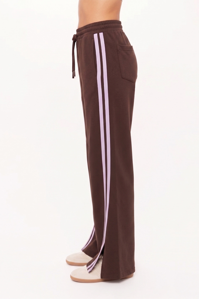 Side profile studio view of a model wearing the high-rise Roma Pant in cocoa. This angle highlights the clean, straight-leg drape of the double-faced jersey fabric and the parallel lilac mesh stripes detailing the side seam.