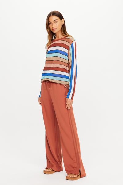 Three-quarter standing view of model Eden wearing The Upside Roma Pant in Desert Rose, styled with a multi-colored striped long-sleeve knit top.