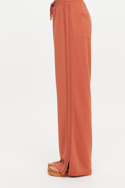 Side profile view of The Upside Roma Pant in Desert Rose showcasing the knitted lace side tape detail and unzipped hem split.