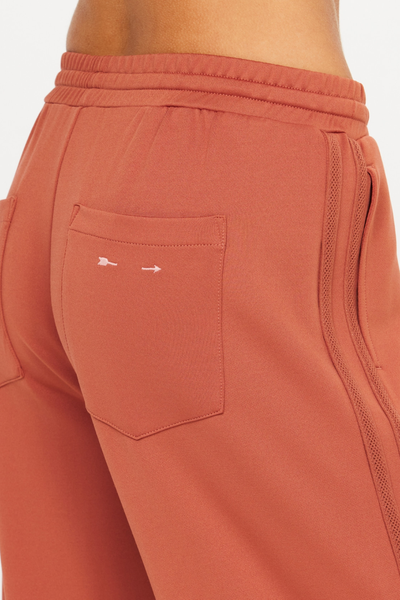 Close-up shot of the right back patch pocket featuring the contrast embroidered arrow logo and knitted lace side trim on The Upside Roma Pant in Desert Rose.