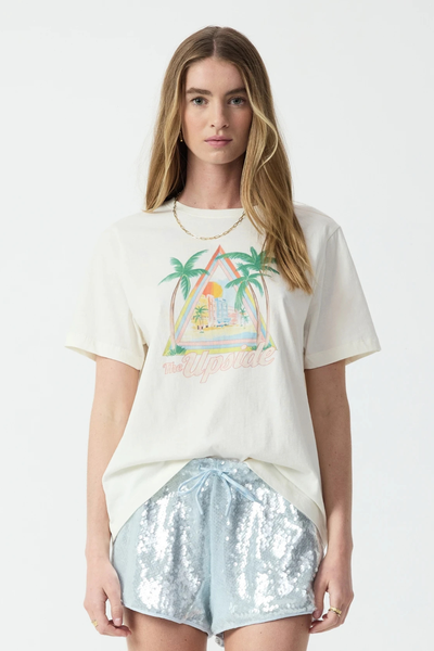 Studio front mid-shot portrait of a blonde model wearing a cream organic cotton Graphic tee styled with light blue sequin athletic shorts and a gold chain necklace.
