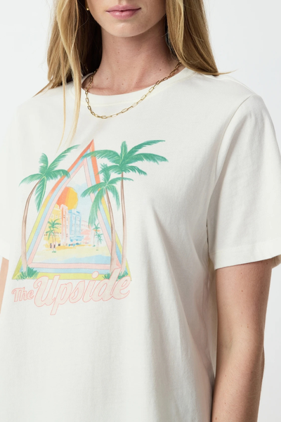 Close-up studio front shot focusing on the crew neck, gold chain necklace, and printed tropical palm tree chest graphic on a cream organic cotton tee.