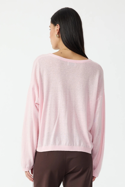 Studio rear view of a model wearing the rosewater pink knit button top and brown trousers against a white background.
