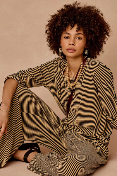 Studio lifestyle portrait of a model sitting down wearing the cream and black stripe set.