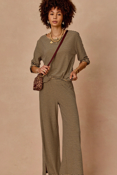 Full-body lifestyle studio view of a model styling the cream and black stripe set with a cross-body bag.