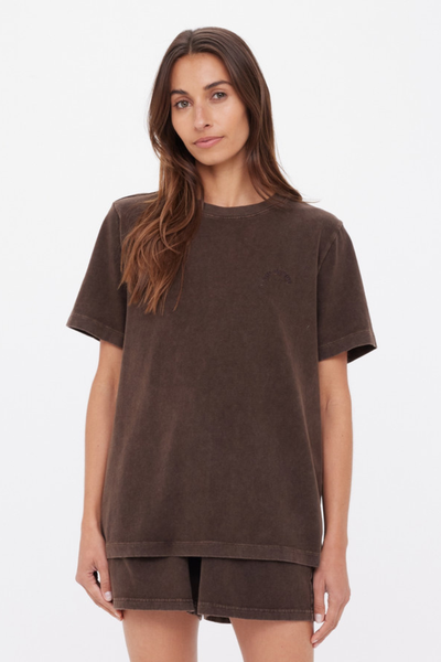 A full-length studio photograph showcasing the relaxed-fit cocoa brown Soho Eva Crew Neck Tee styled as a matching set with tonal lounge shorts and dark flip-flops, emphasizing the shirt's casual proportions and straight hemline.