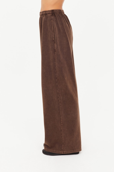 A side-profile studio shot isolating the cocoa brown lounge pants on a model to demonstrate the straight, wide-leg drape and the clean, structural alignment of the side seam pocket detail.