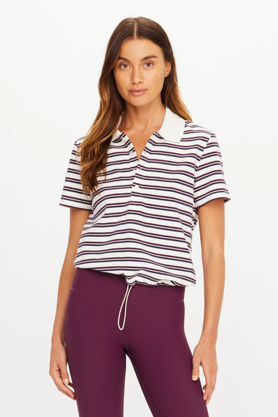 Front portrait view of a model wearing The Upside Sophie Cropped Polo Shirt featuring navy, maroon, and cream horizontal stripes, styled with plum leggings.