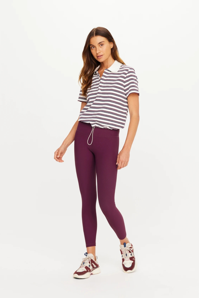 Full-body studio shot of a model wearing The Upside Sophie Cropped Polo Shirt paired with plum activewear leggings and chunky sneakers.