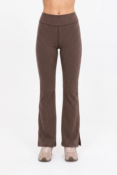 Studio front view of a model wearing the mid-rise geo check flare pants in tan, black, and brown, featuring a soft folded waistband and sneakers.