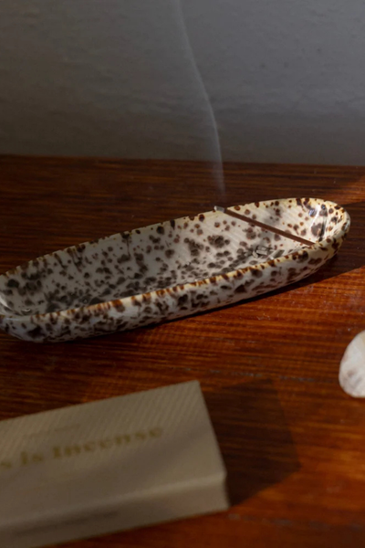 Elevated lifestyle view of the Gentle Habits Collector Ceramic Incense Holder in Leopard print holding a burning incense stick alongside a box of This Is Incense on a warm wooden surface.