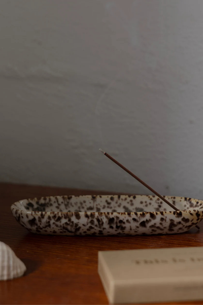 Side profile shot of the Gentle Habits Collector Ceramic Holder in Leopard glaze, resting on a wooden table with a lit burning incense stick and a seashell accessory.