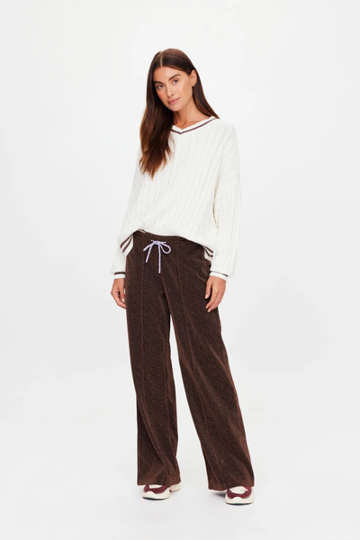 Studio view of a model wearing a cream knit sweater paired with the chocolate metallic wide-leg pants.
