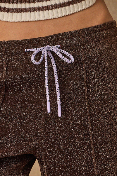 Close-up lifestyle detail shot of the purple paracord drawcord with aglets tied at the waist of the metallic pants.