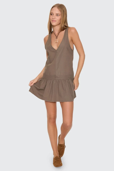 Full-length studio view of a model wearing the olive brown Thrills Avery Mini Dress with a deep V-neckline, drop waist, gathered drop hem, and tan boat shoes.