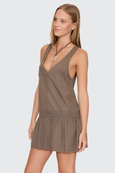 Three-quarter angle studio view of a model wearing the sleeveless Thrills Avery Mini Dress in Olive, highlighting the deep V-neck and drop waist silhouette.