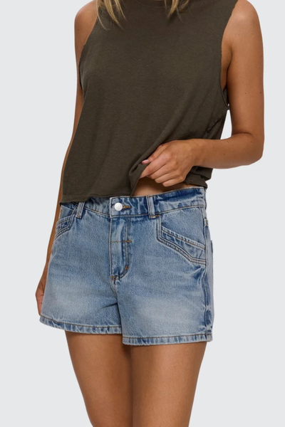Studio front view from the waist down of a model lifting her olive tank top to display sun-washed light blue mid-rise denim shorts featuring western-inspired front pocket stitching.