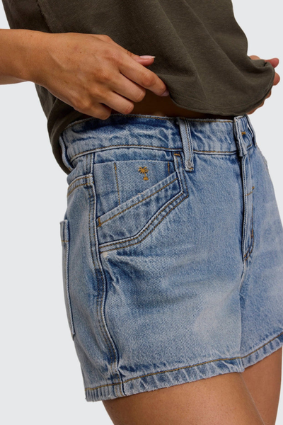Close-up studio side angle of clam bake blue organic cotton denim shorts highlighting the western-style coin pocket with an embroidered palm tree logo and metal rivets.