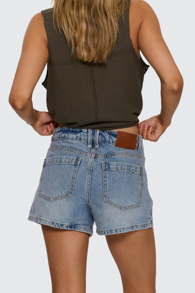 Studio rear view from the waist down of a model wearing light blue organic cotton denim shorts showcasing back patch pockets and a brown leather Thrills logo patch on the waistband.