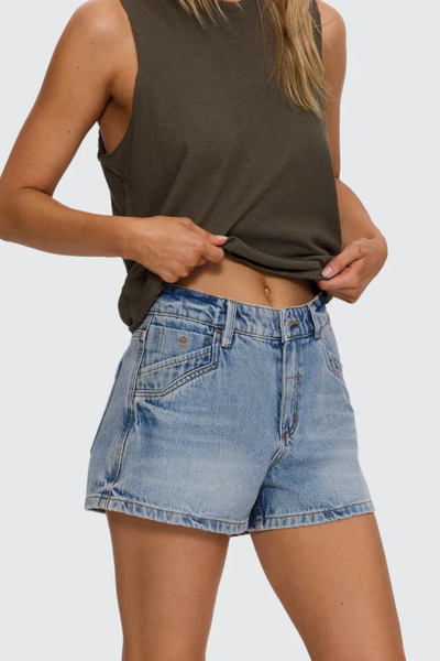 Studio three-quarter front shot from the waist down showing sun-faded light blue denim shorts with western-style pocket paneling and a mid-rise waist.