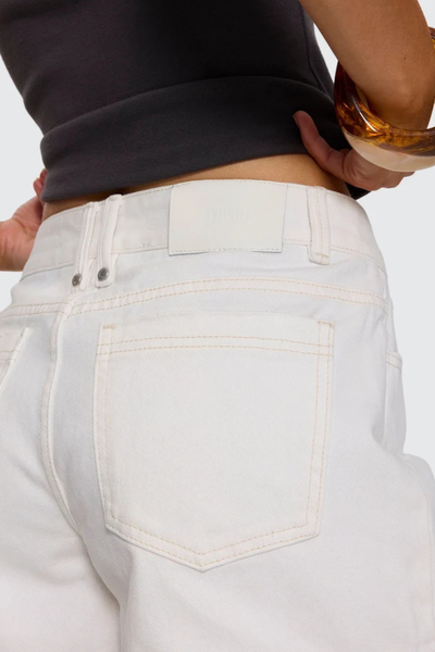Close-up studio rear detail view showcasing the white leather logo waistband patch, double back belt loops, and back patch pocket construction on bright white denim shorts.