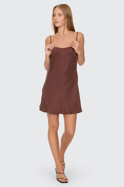 Front view of model holding the adjustable thin shoulder straps of the cocoa brown Thrills Elio Bias Mini Dress, featuring a bias cut silhouette and gathered bust seam.